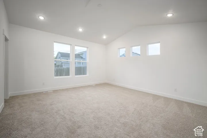 Spacious room featuring vaulted ceilings, recessed lighting, neutral-toned carpeting, and multiple windows