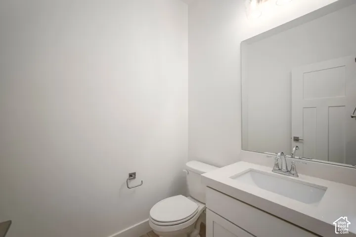 Bathroom featuring a white vanity with integrated sink, a large wall-mounted mirror, brushed nickel fixtures, a white toilet, and wood-finish flooring