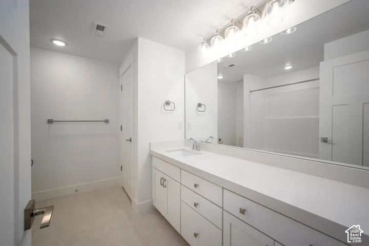 Bathroom featuring a dual vanity with white cabinetry and a light-toned countertop, a large wall-mounted mirror, and a multi-bulb vanity light fixture