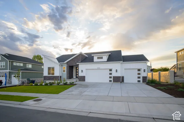 Contemporary exterior featuring white horizontal siding, dark stone accents, a dual garage with modern doors, a partial concrete driveway, and a manicured lawn