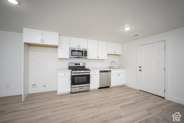 Kitchenette featuring wood-finish flooring, white cabinetry, and stainless steel appliances