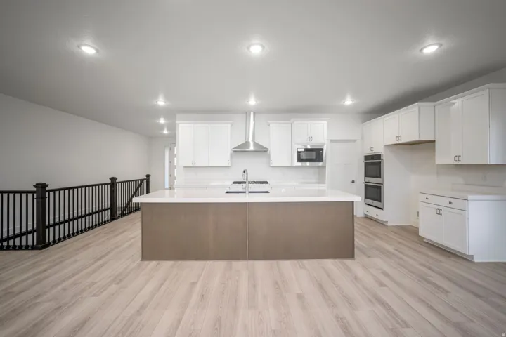Kitchen featuring a large central island with an undermount sink, light wood-finish flooring, white cabinetry, stainless steel appliances, and recessed lighting
