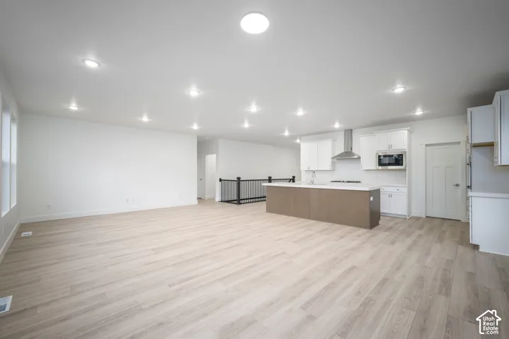 Open-concept living space featuring wood-finish flooring, recessed lighting, and a kitchen with white cabinetry, a central island, and stainless steel appliances including a range hood and microwave