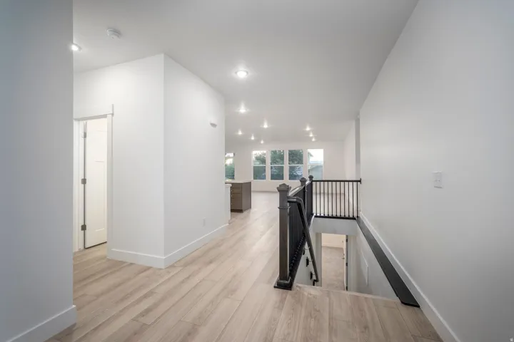Open-concept living space with light wood-finish flooring, recessed lighting, and a dark wood and metal baluster staircase