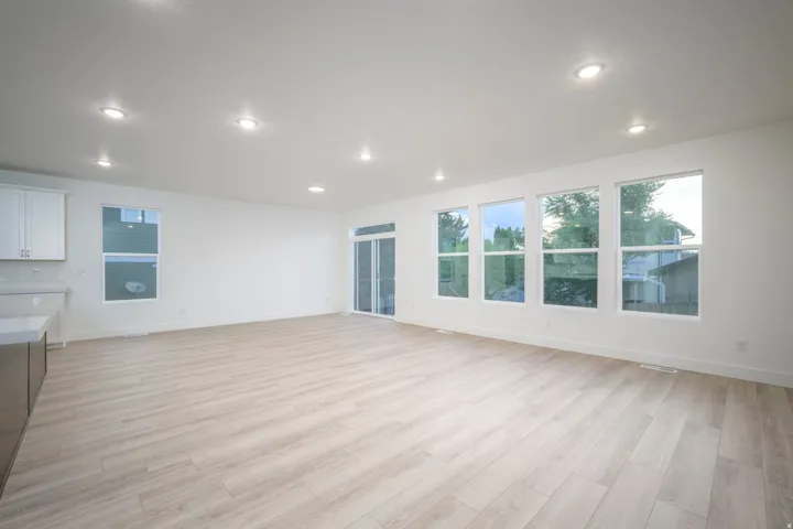 Open-concept living area featuring light wood-finish flooring, recessed lighting, and a wall of four large windows providing abundant natural light