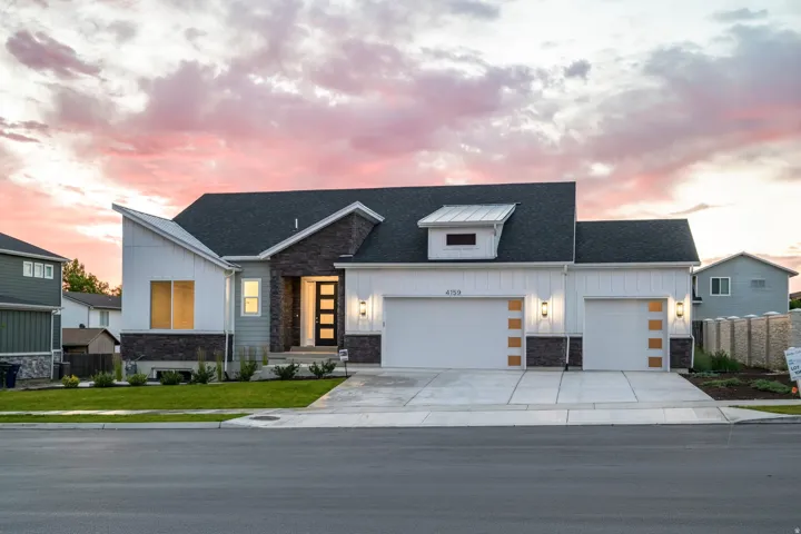 Contemporary facade featuring board and batten siding, dark stone accents, an asymmetric roofline, a multi-pane front door, and an attached two-car garage