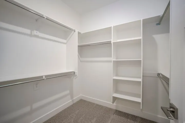 Walk-in closet featuring built-in shelving, multiple hanging rods, and neutral carpet
