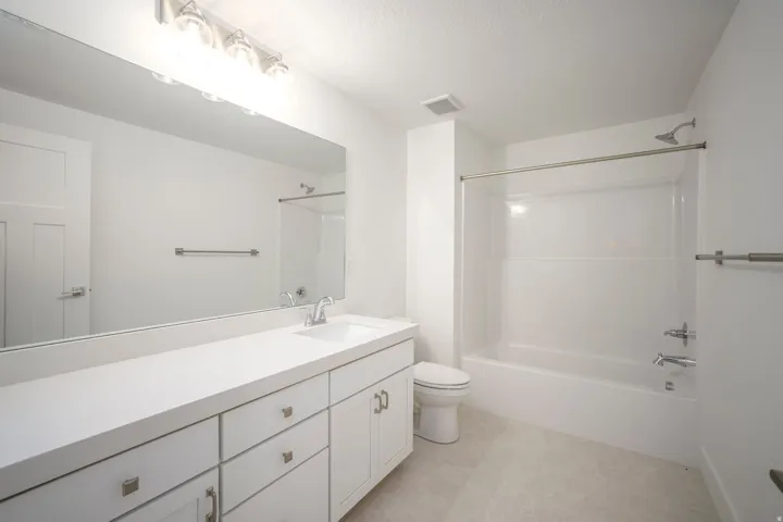 White bathroom featuring an extended vanity with an integrated sink, a large wall-mounted mirror, brushed nickel hardware, and a tub/shower combination