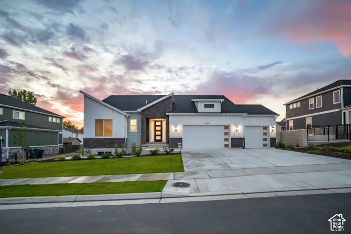 Contemporary exterior featuring mixed material siding, a multi-car concrete driveway, a manicured lawn, an illuminated entry door, and integrated garage lighting