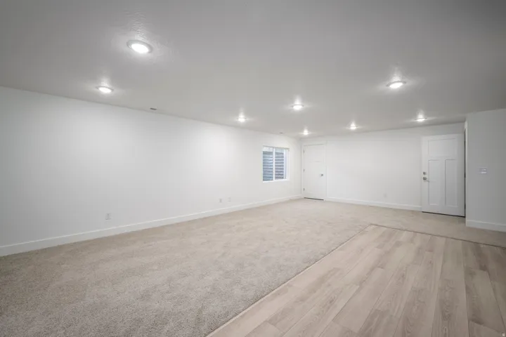 Spacious room featuring light-colored carpeting, wood-finish flooring, recessed lighting, and a window with horizontal blinds