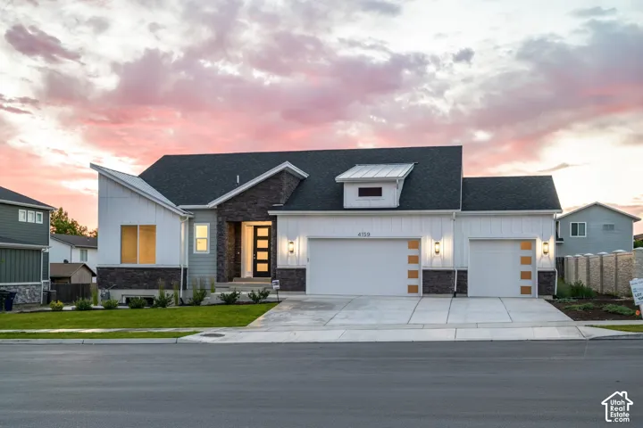 Contemporary facade featuring board and batten siding, dark stone accents, an asymmetric roofline, a multi-pane front door, and an attached two-car garage