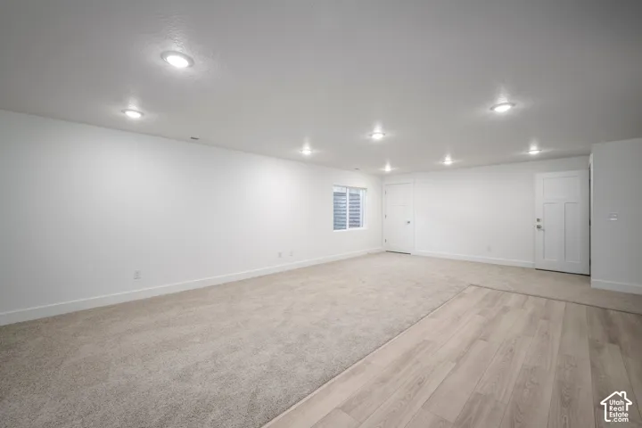 Spacious room featuring light-colored carpeting, wood-finish flooring, recessed lighting, and a window with horizontal blinds