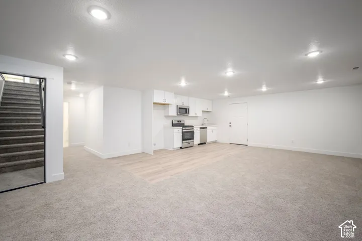 Spacious open-concept room featuring a functional kitchen area with white cabinetry, stainless steel appliances, and a light wood-finish flooring section