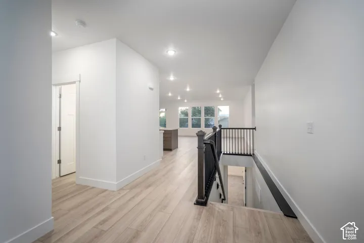 Open-concept living space with light wood-finish flooring, recessed lighting, and a dark wood and metal baluster staircase