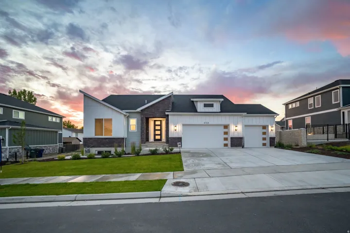 Contemporary exterior featuring mixed material siding, a multi-car concrete driveway, a manicured lawn, an illuminated entry door, and integrated garage lighting