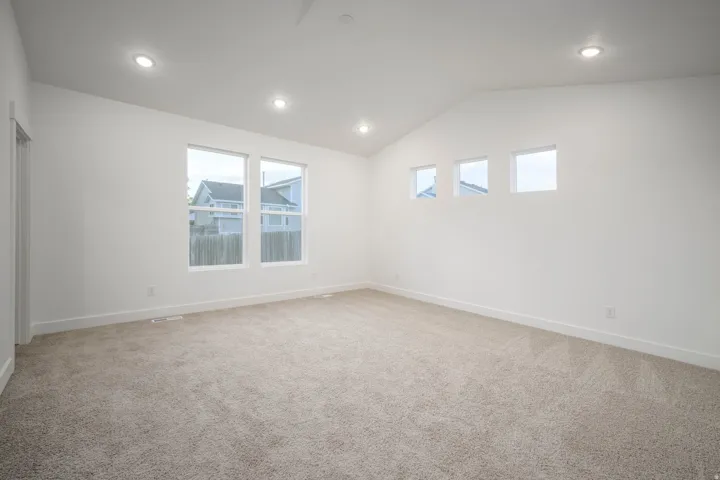 Spacious room featuring vaulted ceilings, recessed lighting, neutral-toned carpeting, and multiple windows