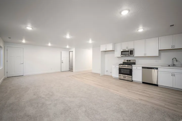 Open concept living area featuring a kitchen with white cabinetry and stainless steel appliances
