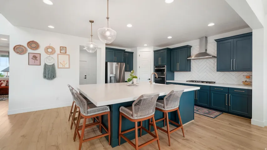 Open-concept kitchen featuring an expansive central island with seating, pendant lighting, shaker-style cabinetry, stainless steel appliances, and wood-finish flooring