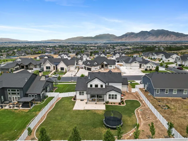 Expansive rear yard featuring a manicured lawn, concrete patio, and white vinyl perimeter fencing