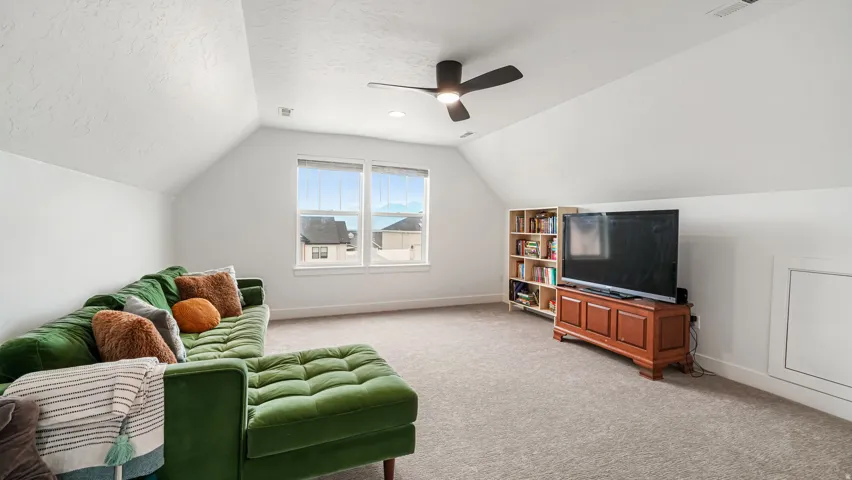 Spacious bonus room featuring sloped ceilings, two large windows, neutral carpet flooring, and a ceiling fan