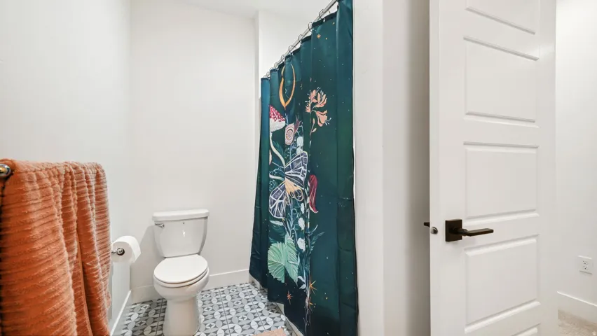 Bathroom featuring a ceramic toilet, patterned floor tiling, and a crisp white three-panel door with matte black hardware