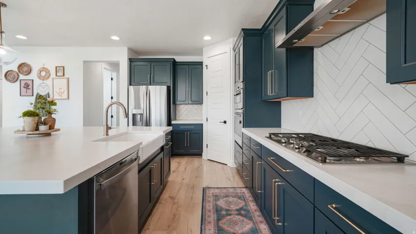 Contemporary kitchen featuring deep teal cabinetry, light-toned countertops, and wood-finish flooring