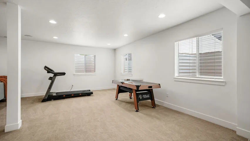 Spacious room featuring light-colored carpeting, multiple windows with blinds, recessed lighting, and a neutral wall color throughout
