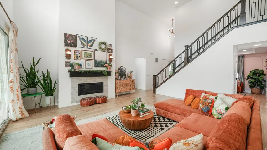 Open-concept living area featuring a two-story ceiling, wood-finish flooring, and a fireplace with a light-colored stone surround and dark mantel
