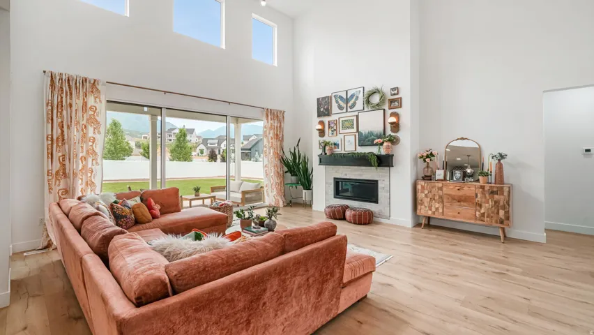 Spacious living area featuring high ceilings with upper transom windows, light wood-finish flooring, and a fireplace with a light stone surround