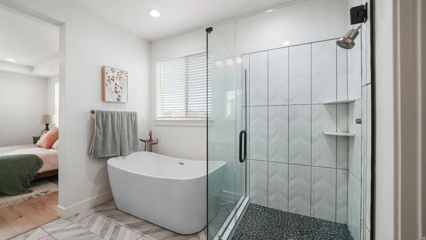 Bathroom featuring a freestanding soaking tub with bronze-finish fixtures, a glass-enclosed shower with chevron-patterned wall tile, and a pebble-stone shower floor