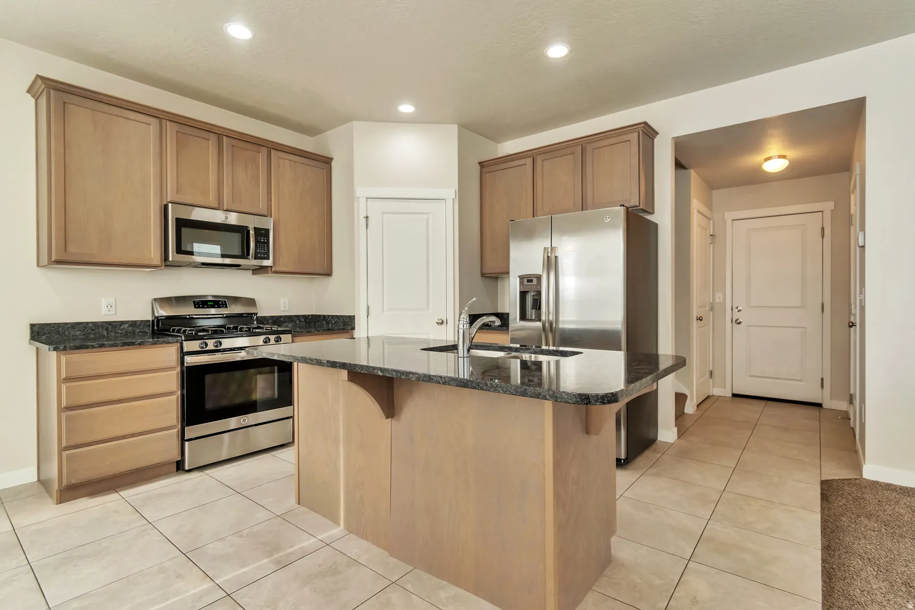 Kitchen featuring stainless steel appliances, wood-finish cabinetry, dark stone countertops, a central island, and tile flooring