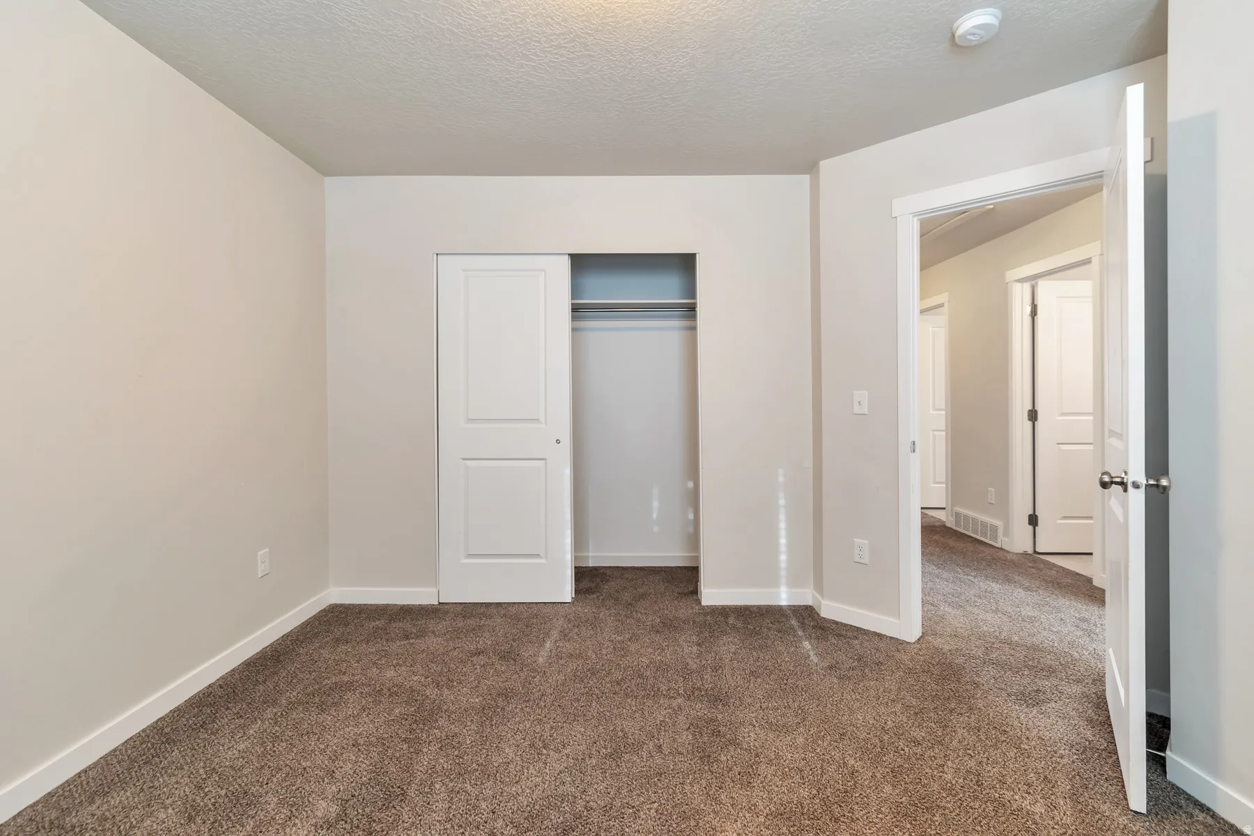 Room featuring neutral-toned walls, brown carpet flooring, and a closet with sliding panel doors