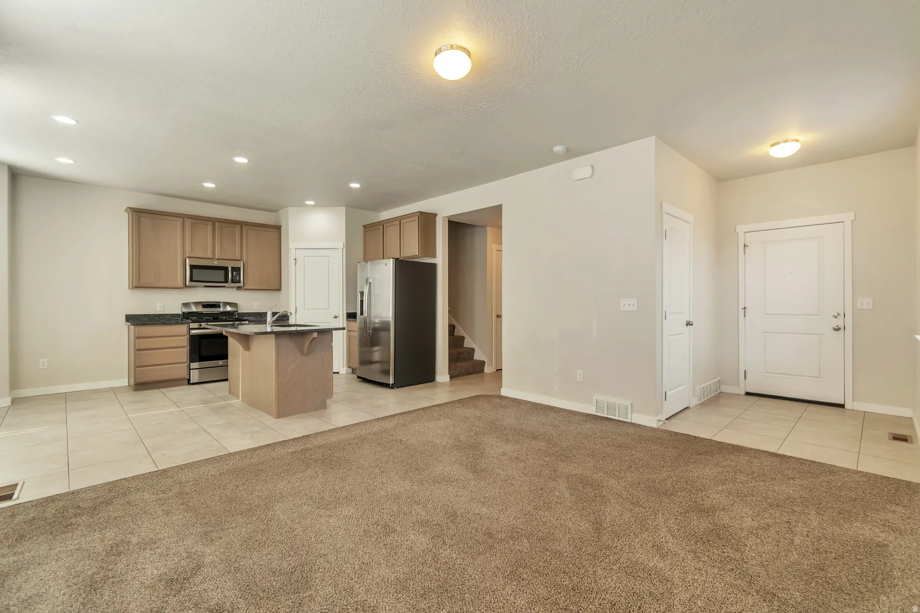 Kitchen and living area combination featuring a central island, stainless steel appliances, light wood-finish cabinetry, and recessed lighting