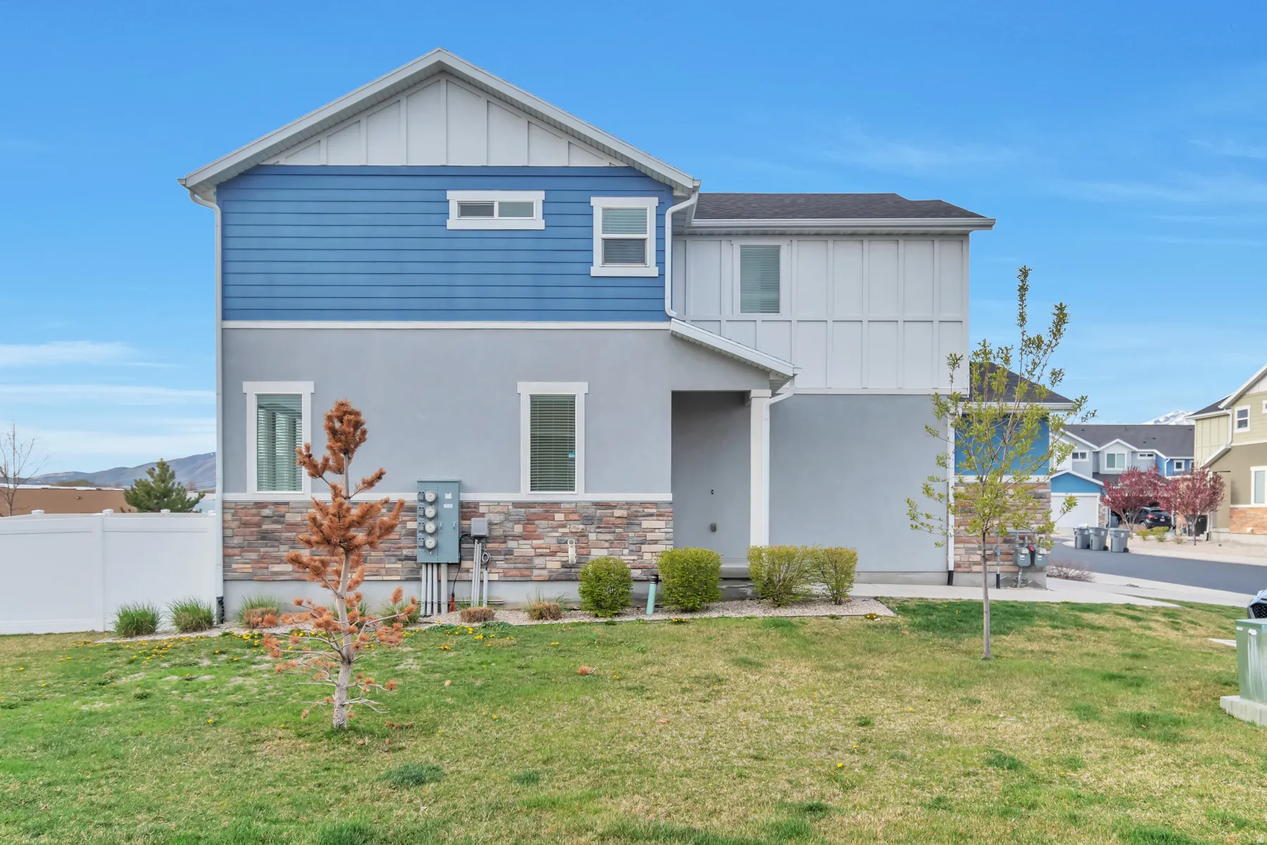 Contemporary residential exterior featuring blue horizontal siding, light gray stucco, and a stacked stone foundation