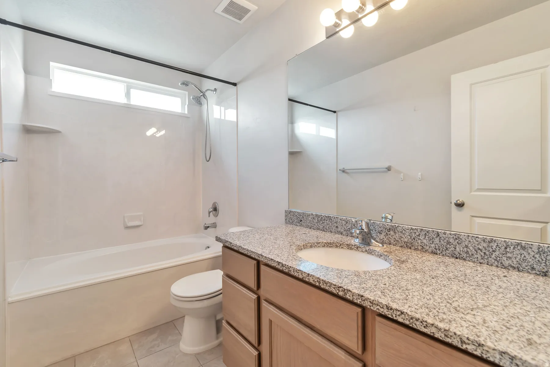 Bathroom featuring a spacious vanity with a light granite countertop and undermount sink, ample cabinetry, a full-width mirror, and a tub-shower combination with a high window