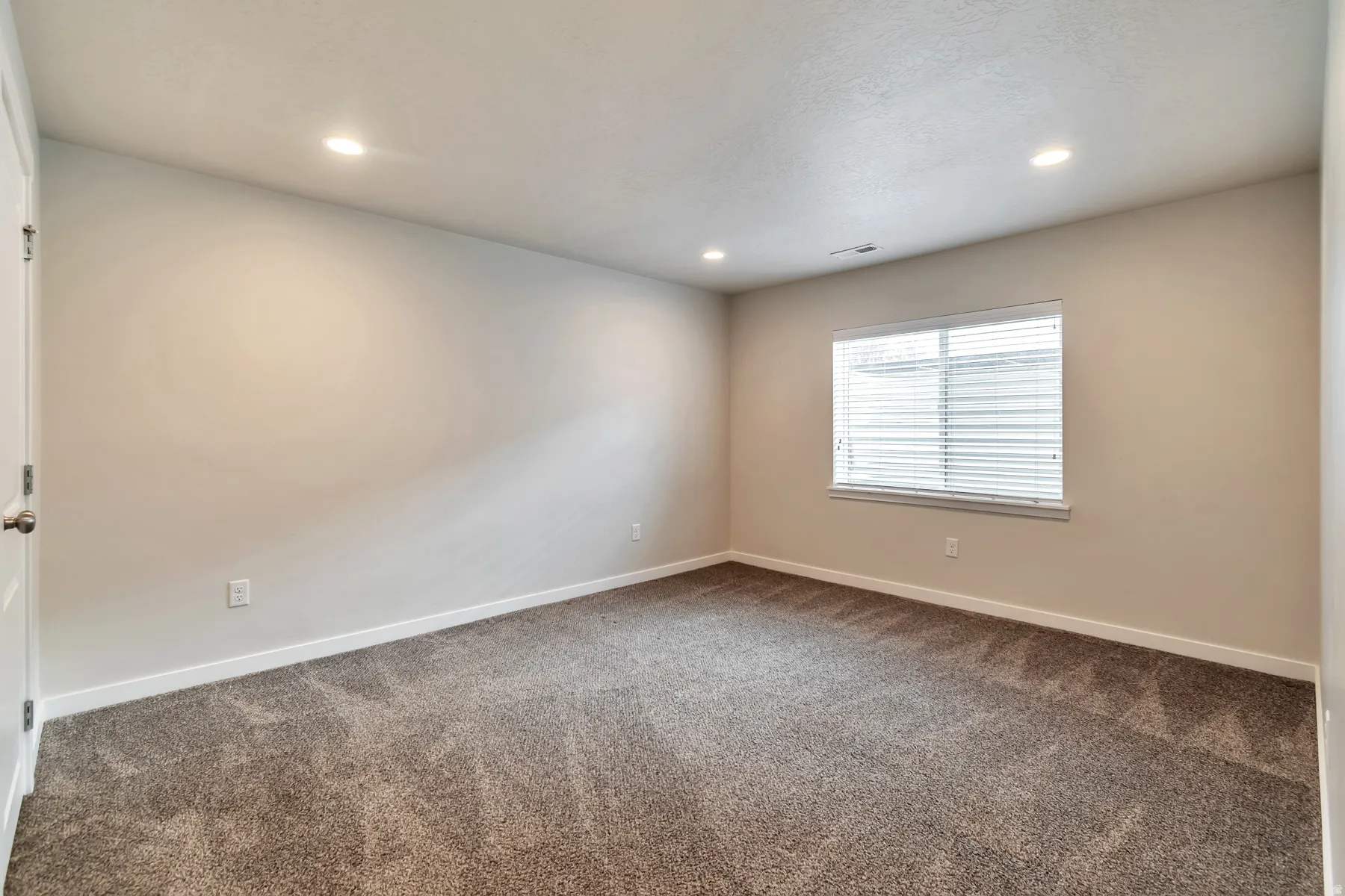 Neutral-toned room featuring a single window with blinds, recessed ceiling lighting, and light brown carpeting
