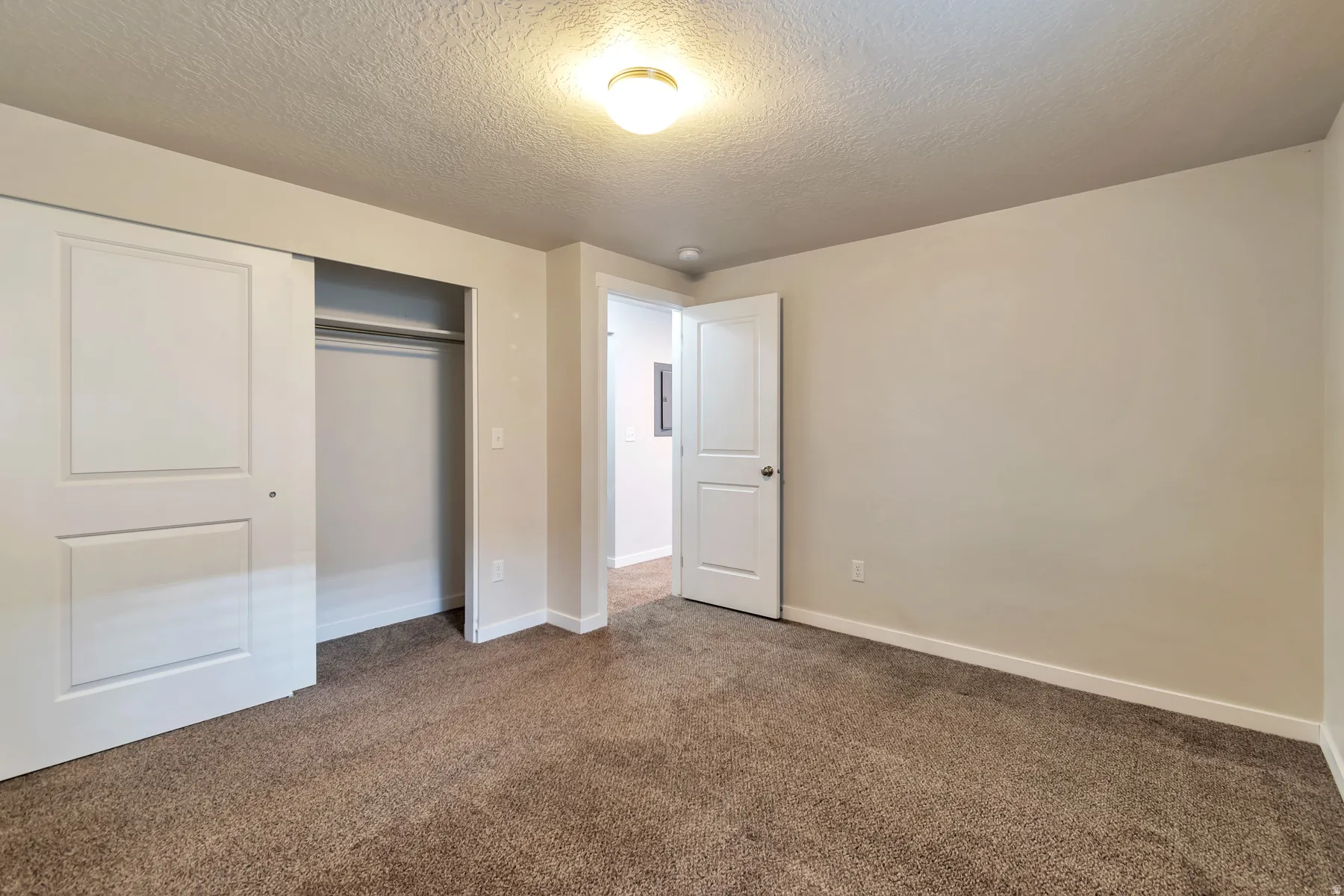 Spacious room featuring neutral carpeting, light-toned wall paint, and a built-in closet with sliding panel doors