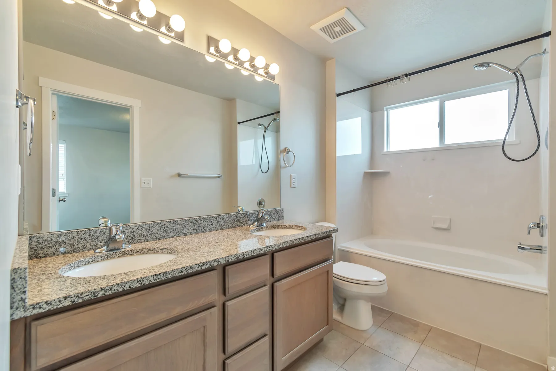 Bathroom featuring a double vanity with granite countertop, wood-finish cabinetry, and contemporary light fixtures
