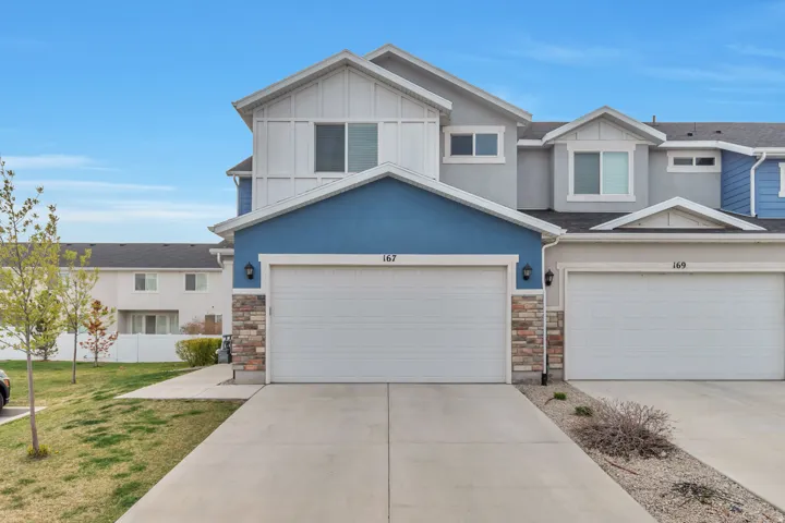 Modern stucco exterior with board and batten accents, dual garage doors, decorative stone veneer, and a concrete driveway