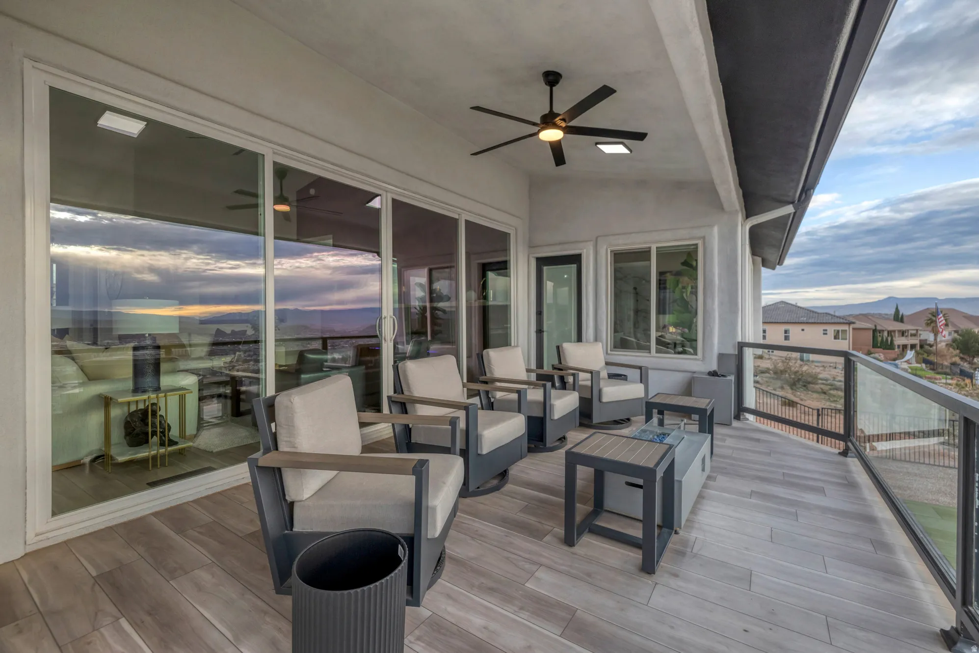 Expansive outdoor balcony featuring wood-finish flooring, a ceiling fan with integrated lighting, and multiple sliding glass doors