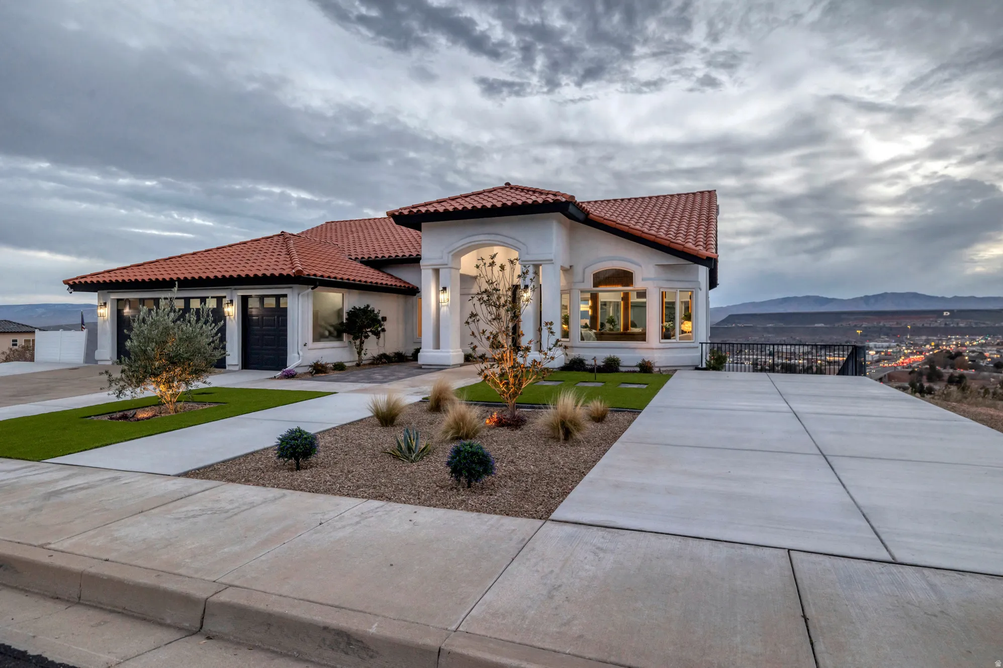 Stucco exterior residence featuring a red tile roof, arched entryway with columns, and a two-car garage with dark paneled doors