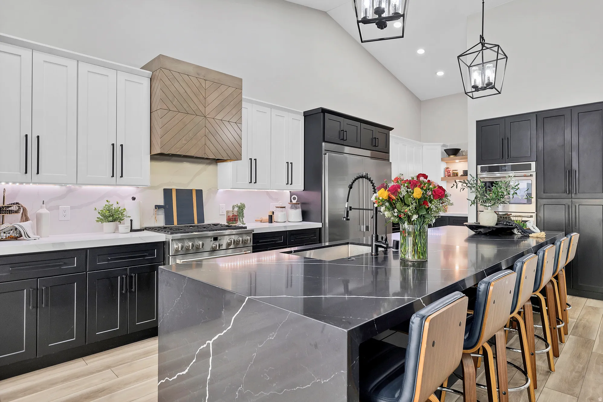 Spacious kitchen featuring a waterfall island with seating, stainless steel appliances, two-tone cabinetry, a decorative wood range hood, and vaulted ceilings