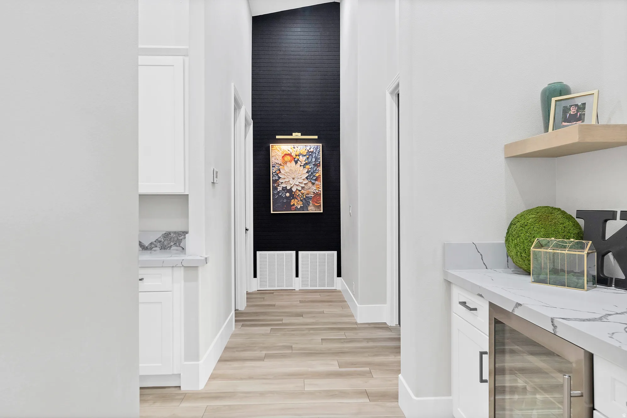 Hallway featuring wood-finish flooring, a tall black accent wall with a unique texture, and a built-in wet bar with a beverage refrigerator