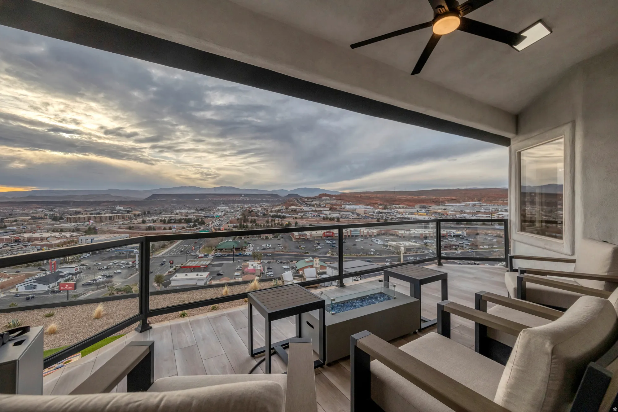 Expansive covered balcony featuring glass panel railing, wood-finish flooring, and a modern ceiling fan with integrated lighting