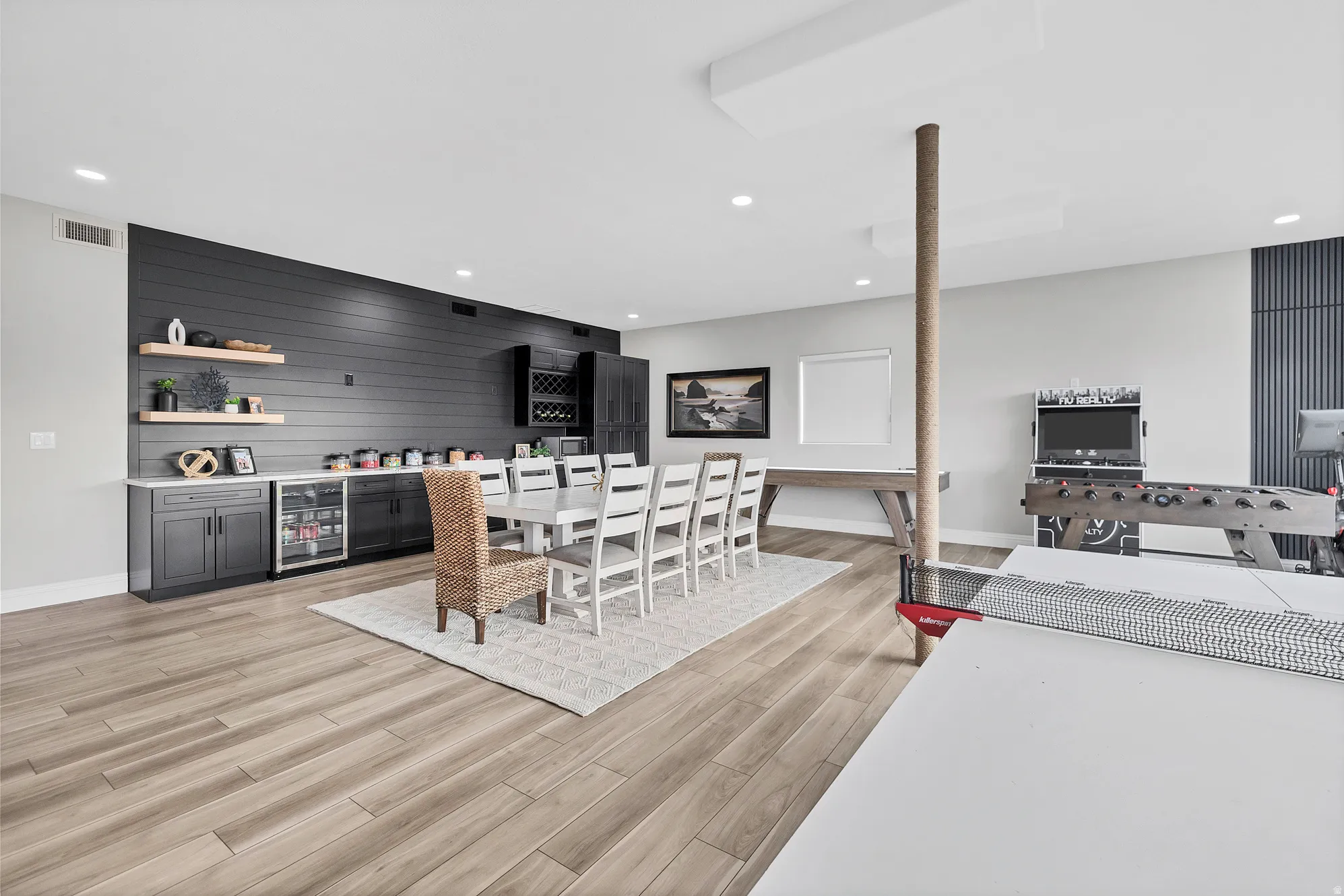 Spacious entertainment area featuring wood-finish flooring, recessed lighting, and a modern beverage bar with built-in cabinetry and open shelving
