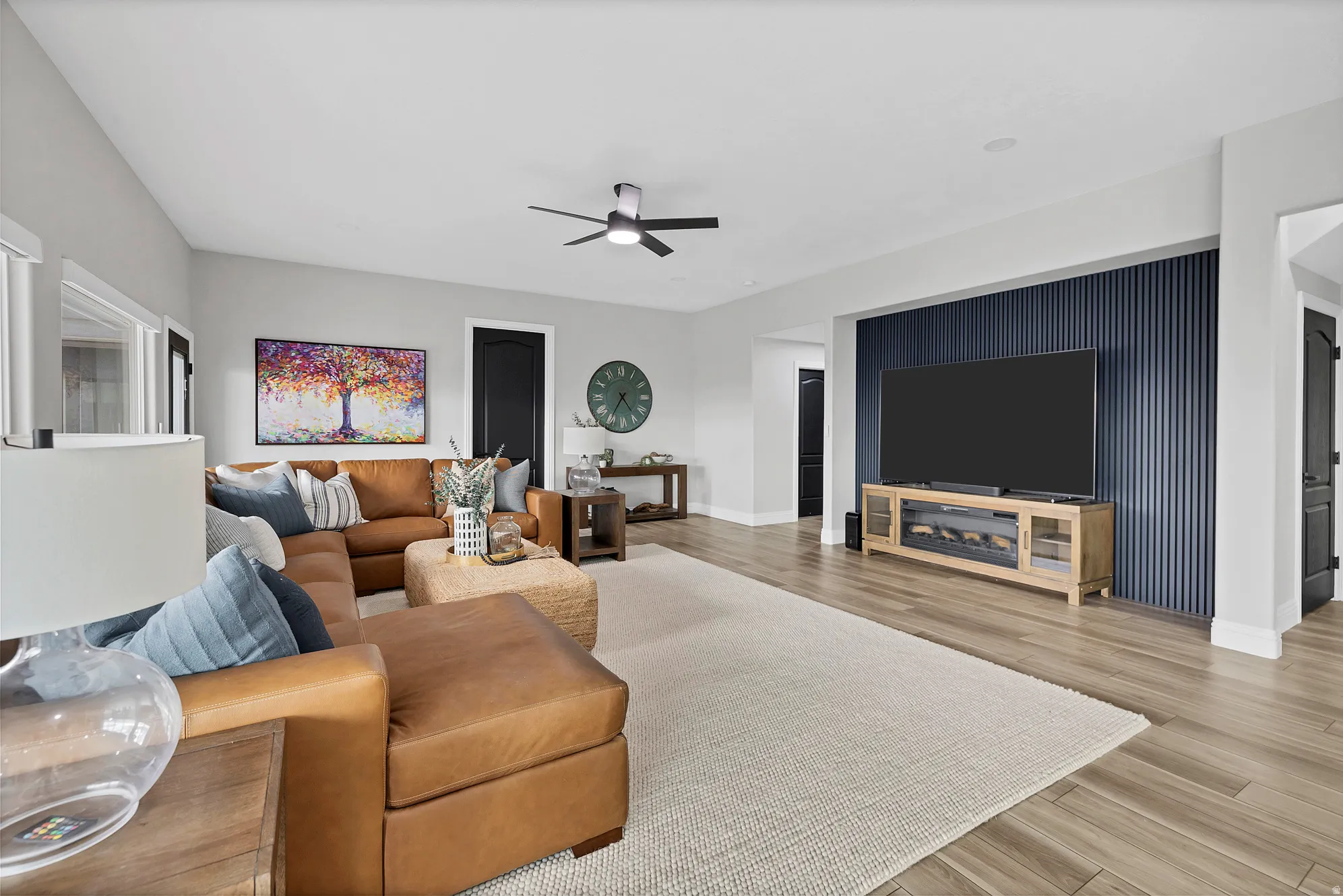 Spacious living area featuring wood-finish flooring, a contemporary ceiling fan, and a prominent accent wall with vertical paneling