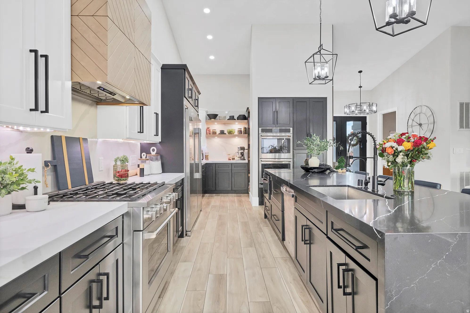 Gourmet kitchen featuring a waterfall island with an integrated sink, stainless steel appliances, custom cabinetry, wood-finish flooring, and recessed and pendant lighting
