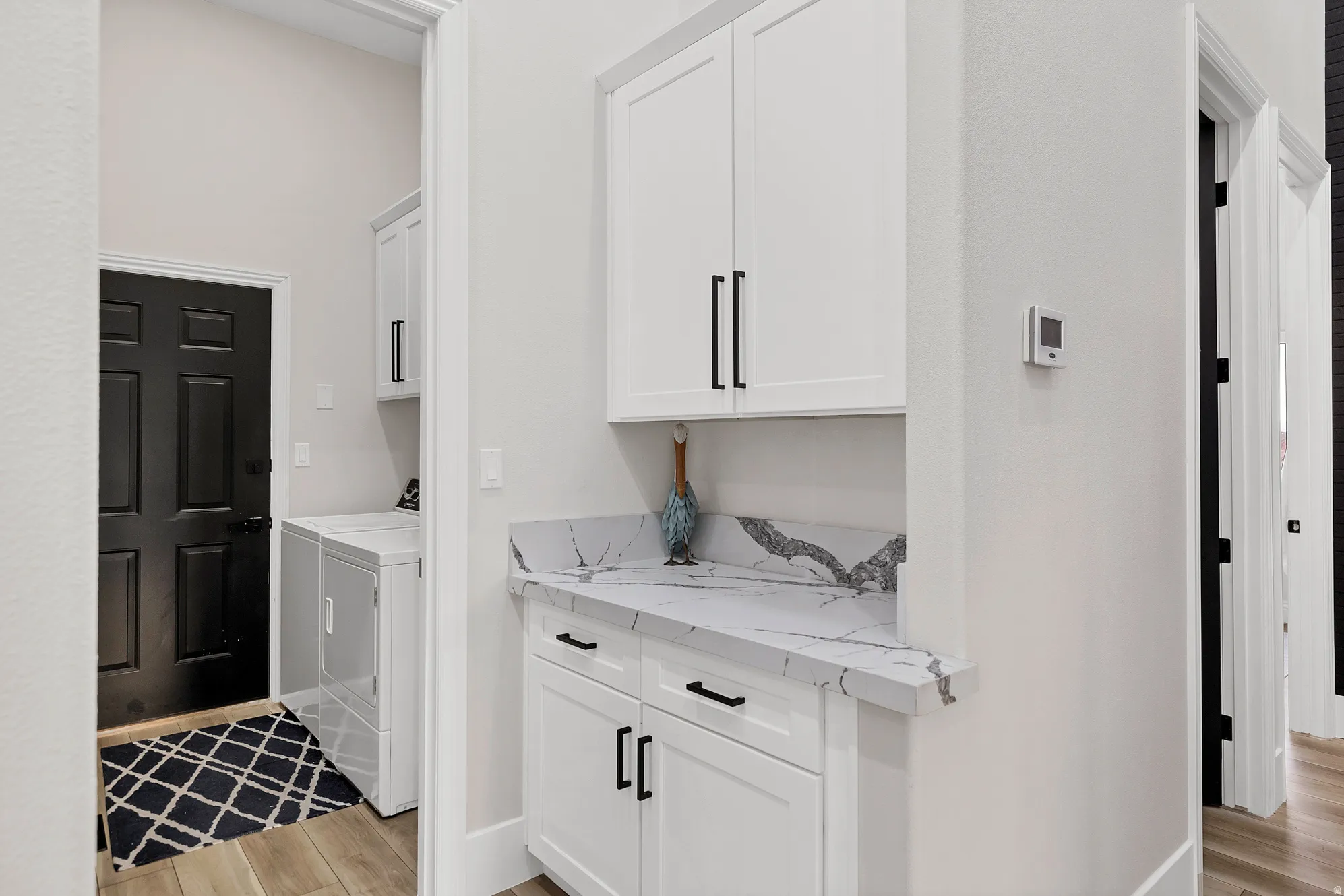 Laundry area featuring white cabinetry, black hardware, and a marble-finish countertop with a matching backsplash
