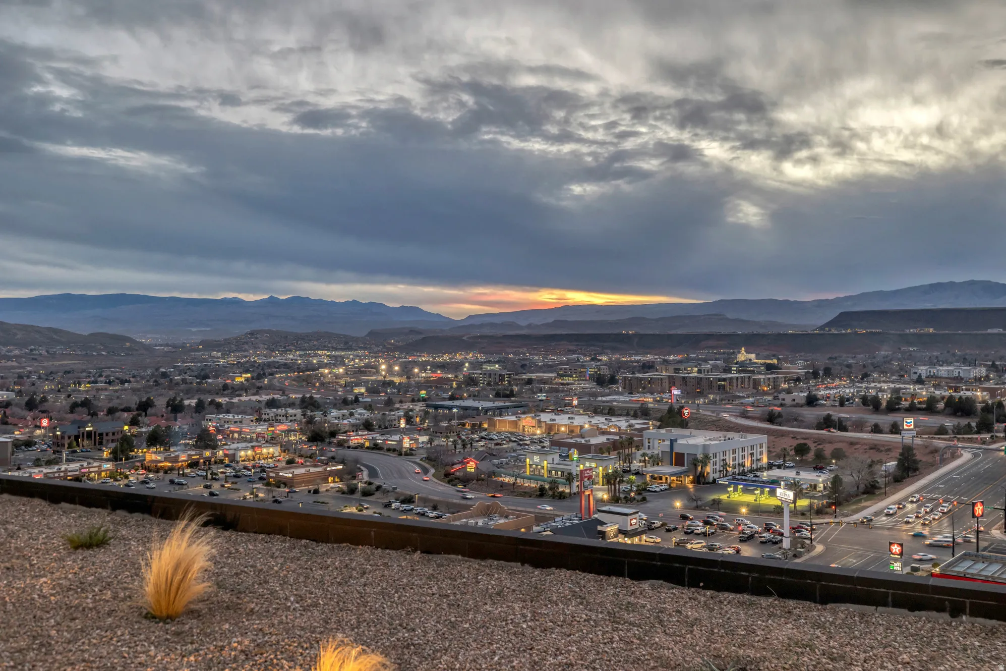 Expansive city skyline with illuminated buildings and infrastructure, framed by distant mountains