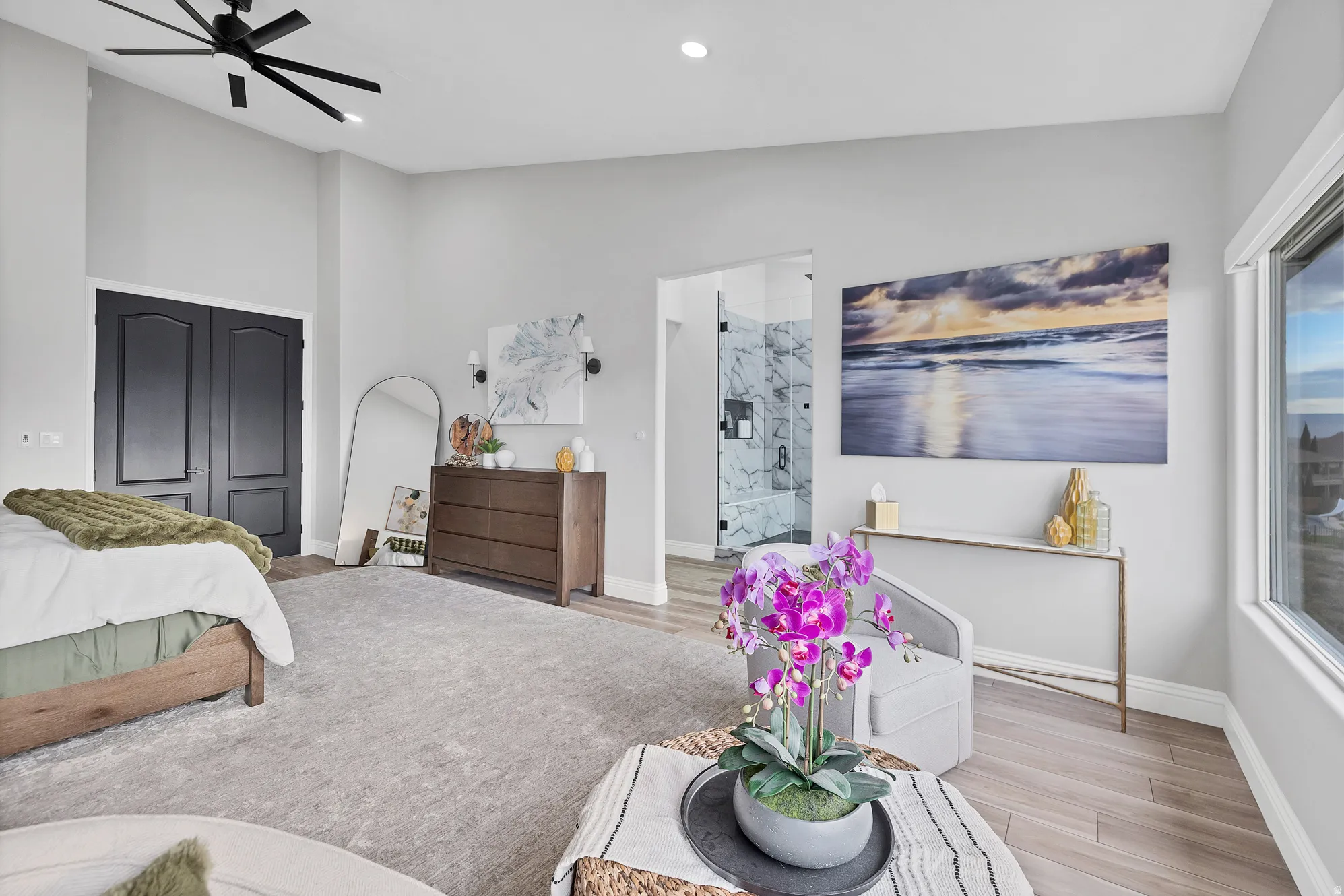Spacious sleeping area featuring vaulted ceilings, a modern black ceiling fan, light-toned wood-finish flooring, and large windows